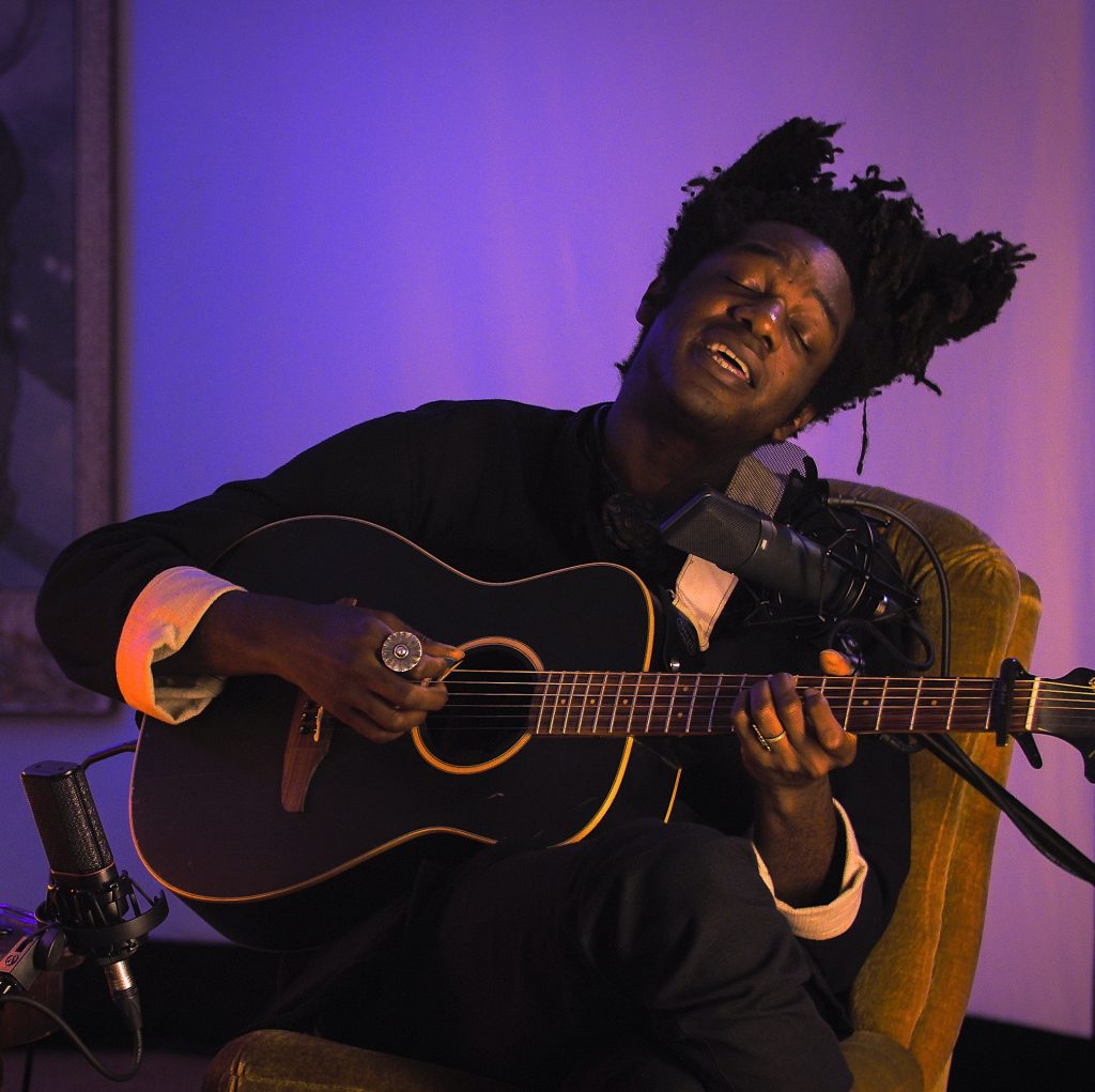 L.A. Salami sings and plays guitar from a chair